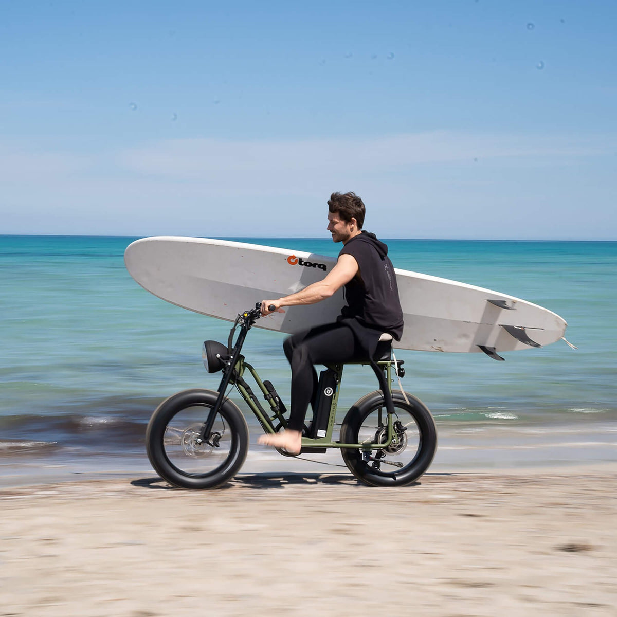 Rider carrying a surfboard on a Unimoke SW along the beach